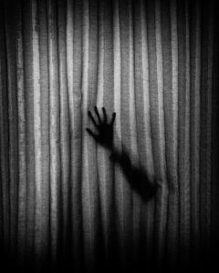 Hand silhouette behind curtain. Photo by Darkness on Unsplash