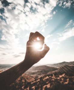 Hand against sky with sun coming through fingers. Photo by Daoudi Aissa on Unsplash.