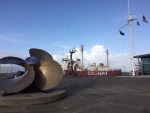 Boat against a blue sky with a propeller displayed in the foreground.