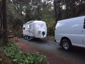 White van and trailer in the forest.