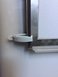A white catch is clamping the bottom corner of a door to hold it open.