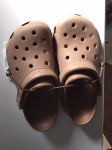 Tan pair of Crocs secured to a white wall with a mini bungee connected by two hooks.