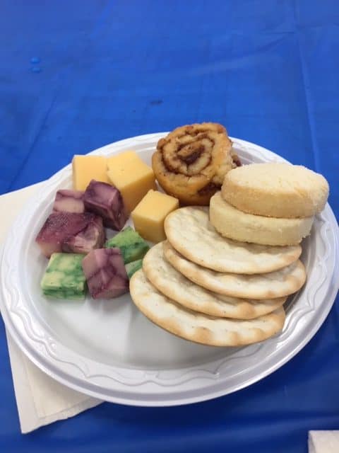 White paper plate with round crackers, cookies and three kinds of cheese. 