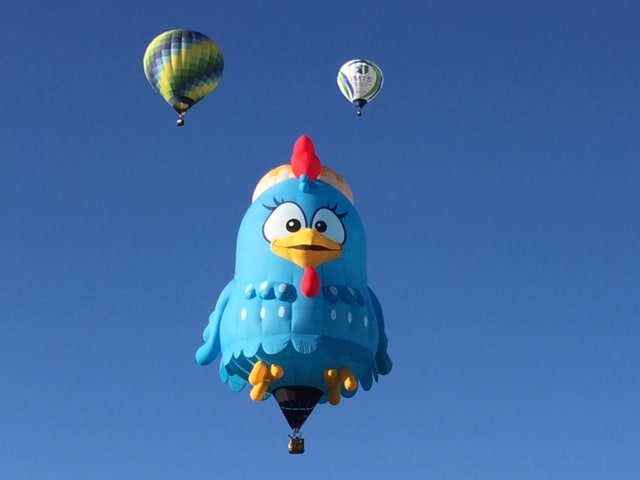 Hot air balloon shaped like a little chicken, flying against a blue sky.