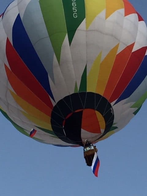 Close up of a hot air balloon with the white, blue, red Russian flag flapping in the air from the basket.