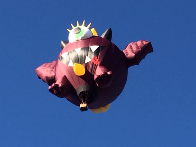 Purple round hot air balloon against dark blue sky. Has wings, one eye and a horn on top.
