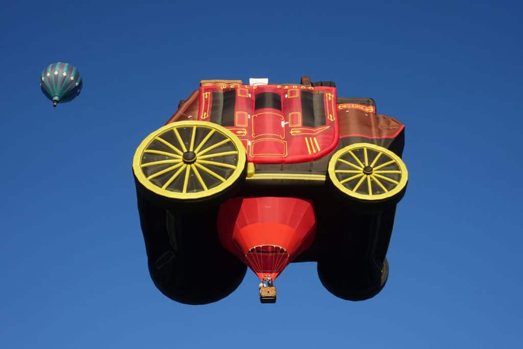 Hot air balloon in the sky. It is the Wells Fargo wagon. Old fashioned horse driven way, red with yellow wheels.