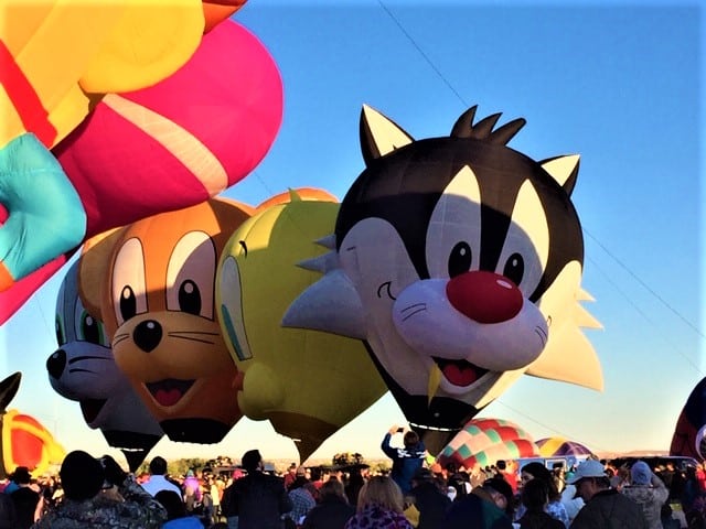 Hot air shapes balloons in the shape of Looney Tunes, still on the ground, with people all around.