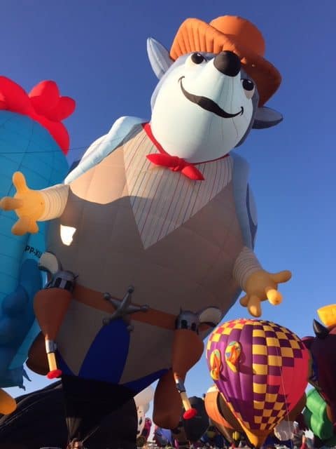 Hot air balloon in the shape of an armadillo dressed as a cowboy on the launch field.