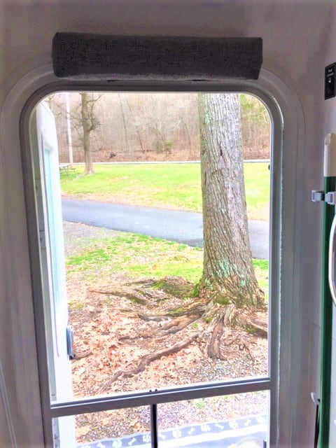 Taken from inside the doorway of the Oliver Trailer looking out at grass and trees. Above the door frame is a pad the width of the door.