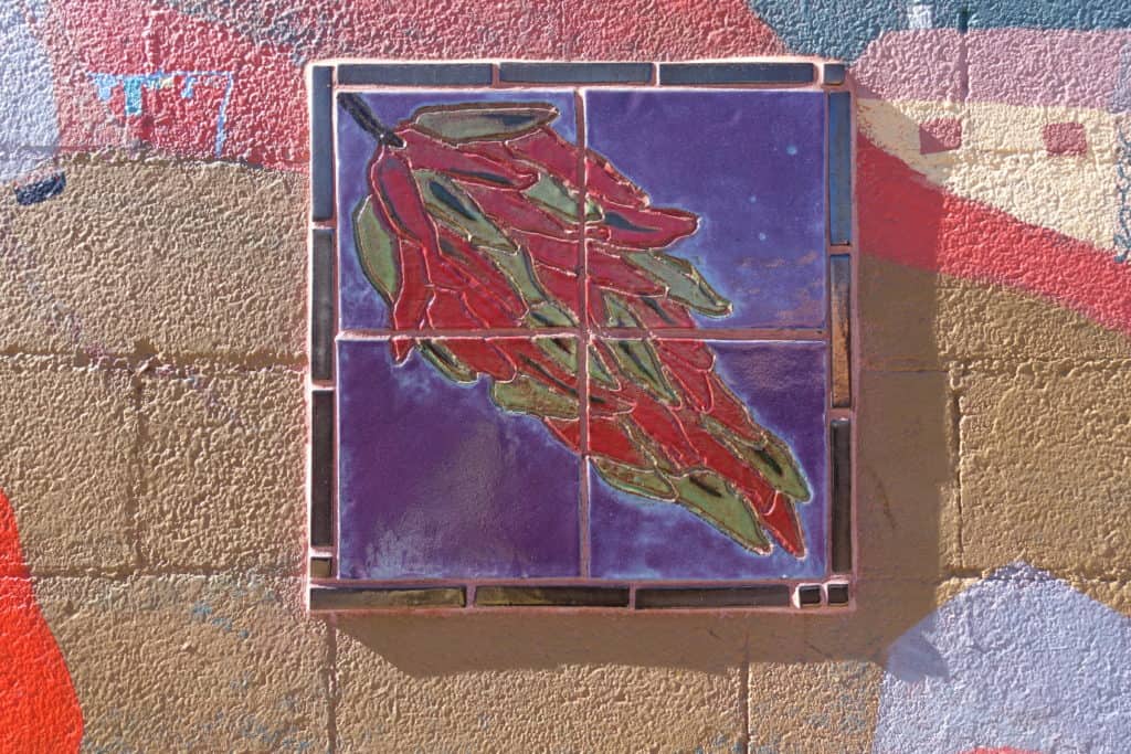 Four painted tiles put together to form a square. The painted picture is red and green chiles on a purple background.
