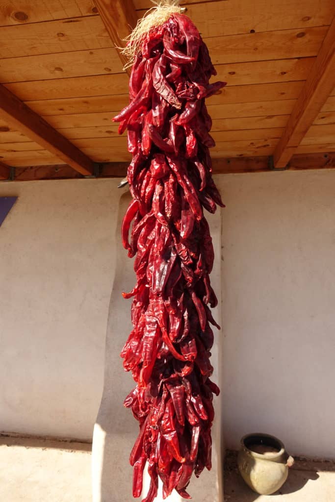 A long string of dried red chiles hanging outside from the  roof of a building's overhang.