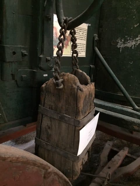 Close up on one part of chuck wagon, a wooden box hanging by a chain from the side of the wagon.