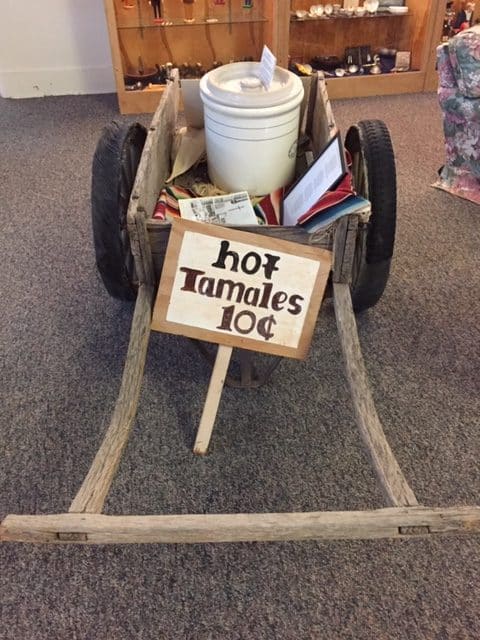 A wooden hand cart with a white bucket in the back and a sign that says, "hot tamale 10 cents."