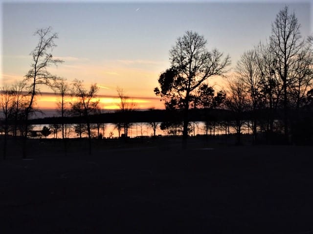 A sunset over a lake with outlines of trees.