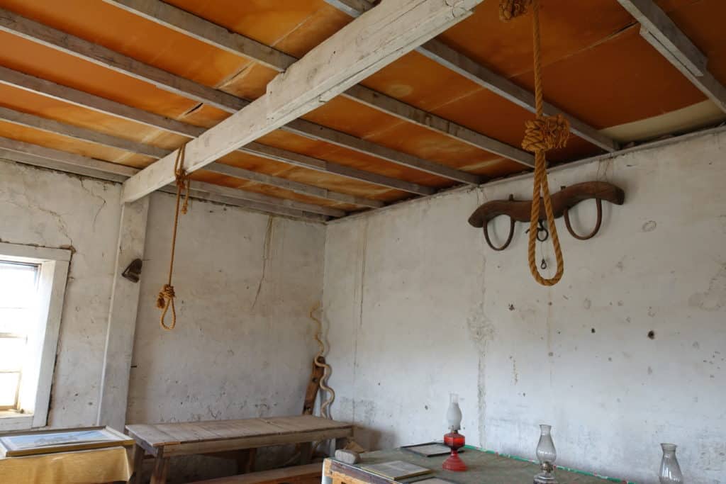 Old empty room with white walls and beams across ceiling. Two ropes tied in a noose hanging down.