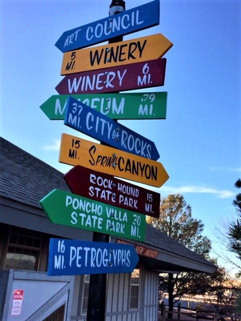 A colorful sign post taken against a blue sky. It includes 9 directional markers to places to visitor in and around Deming, New Mexico.