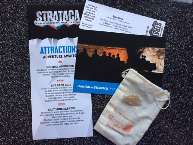 On a black speckle table, a brochure, entry ticket, postcard and a little white sack with a piece of salt rock on it.