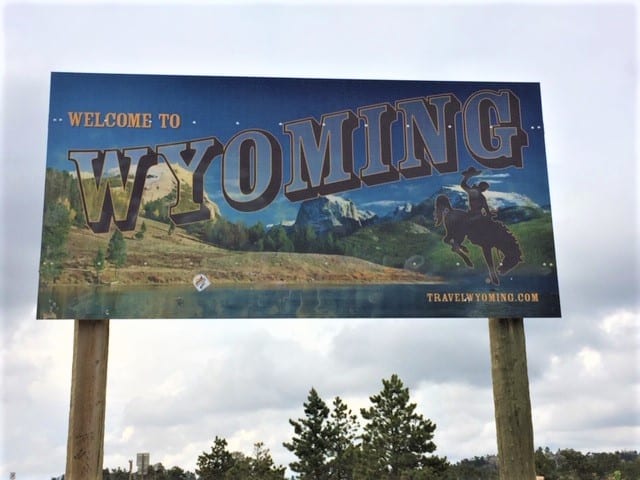Road sign along a highway that reads "Welcome to Wyoming." Sign has mountains and the state logo of a cowboy on a bucking bronco.