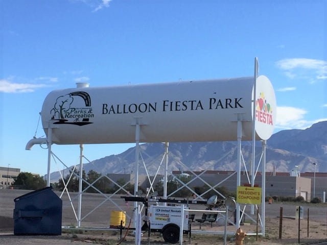 A vertical tube-shaped water tower with words Balloon Fiesta Park on the outside.