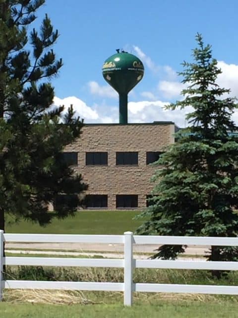 A dark green water tower coming up behind a building. You can only see half of the writing and it's blurry. Trees frame the photo.
