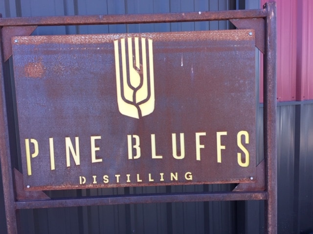 Close up of a brown metal sign with Pine Bluffs distilling stenciled on in light yellow.  