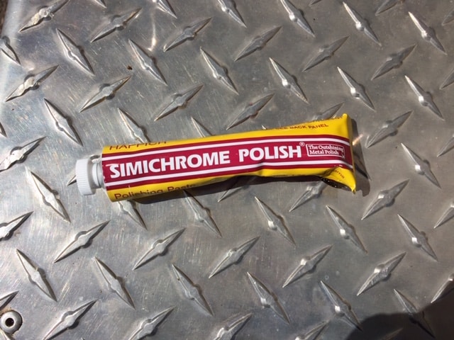 Photo of the tube of polishing paste sitting on a textured bumper. Tube is yellow and red with write writing. It says Simichrome Polish.