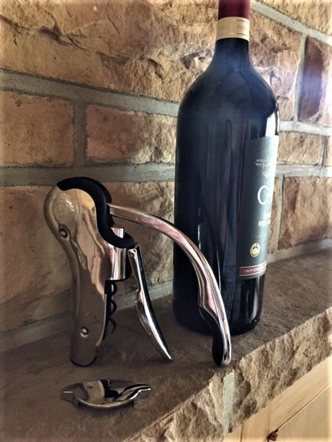 On a rock ledge, a bottle of wine with a rabbit-type bottle opener.
