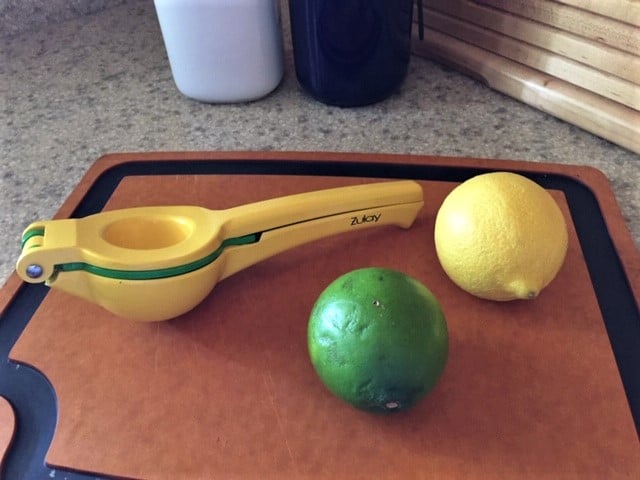 A cutting board with a whole lemon and a whole lime. Then a hand-held juice sitting next to them.