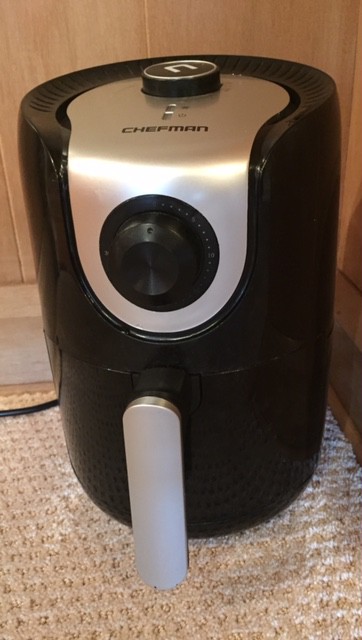 A black and silver air fryer kitchen appliance in the corner against a wood panel background.