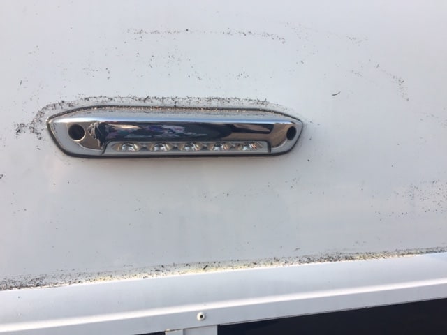 Close up of an outside light on an RV as well as the top rim of a window covered in gray and black ash flecks. 