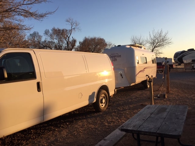 White white and white trailer in a dirt campground. Photo has a yellow glow from setting sun.