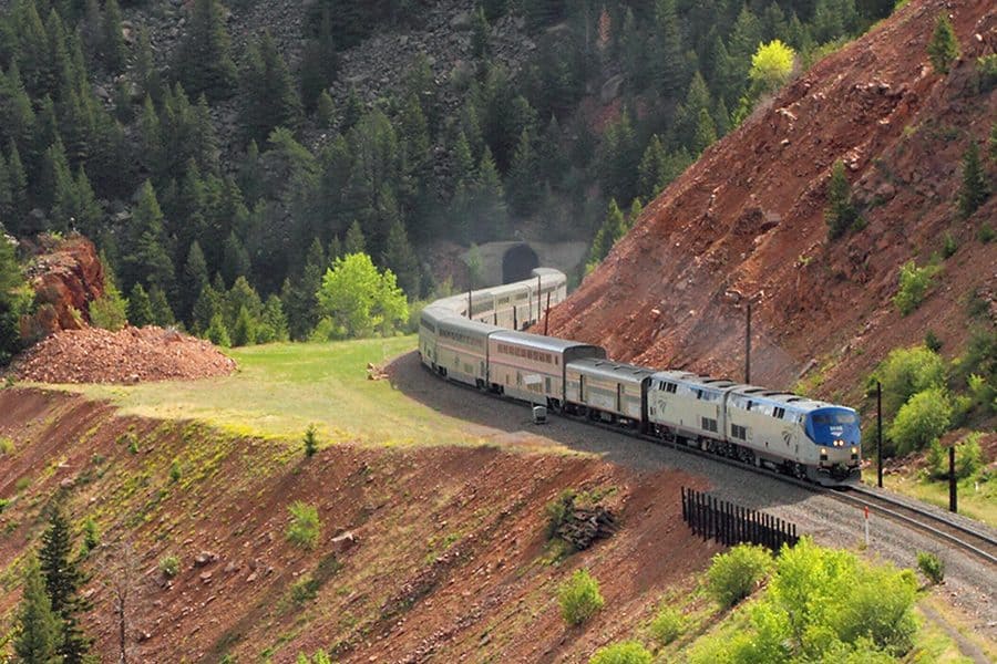 A silver train rounding a mountain.