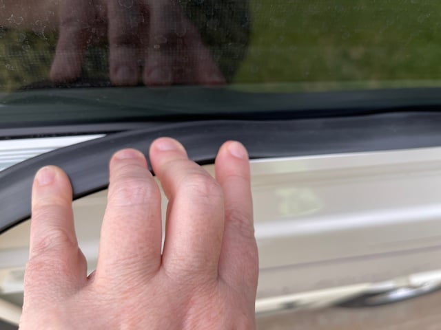 Person's fingers pushing in the black window seal of an RV window frame.