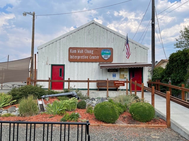 White building with two red doors. Signage says Kam Wah Chung Interpretive Center.