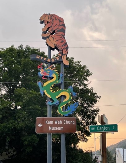 Directional sign to Kam Wah Chung Museum with a dragon above it and a tiger above that.