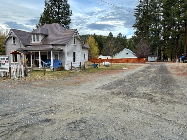 A large dilapidated gray house with a gravel road going by. In the background are other structures.