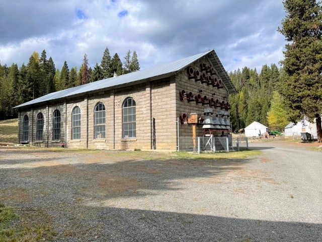 Large stone building with large windows in front of lots of pine trees.