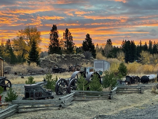 Wheels and other mechanical parts displayed along a road at sunrise.