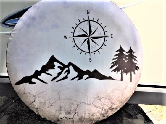 RV tire cover with mountains, trees and a compass.