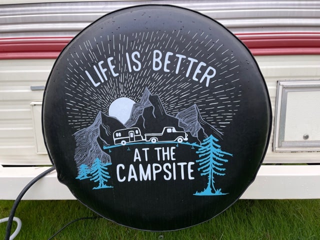 RV tire cover with mountains, trees and an RV that reads Life is Better at the Campsite. 