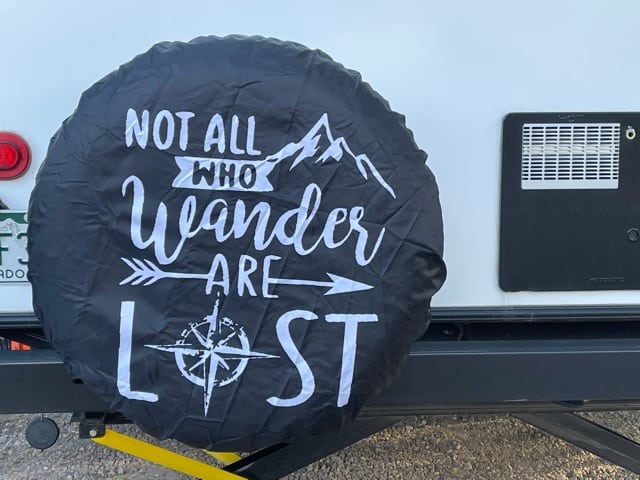 RV tire cover with mountains, an arrow and a compass that reads Not All Who Wander Are Lost.  