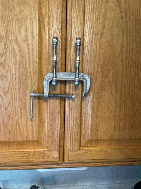 Close up of wooden cabinet doors in an RV. A c-clamp threaded through the handles to make sure they don't accidently open.