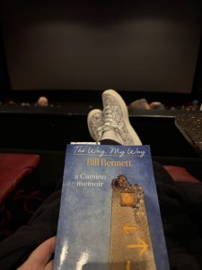 Book on a person's lap with their feet up in a movie theater.